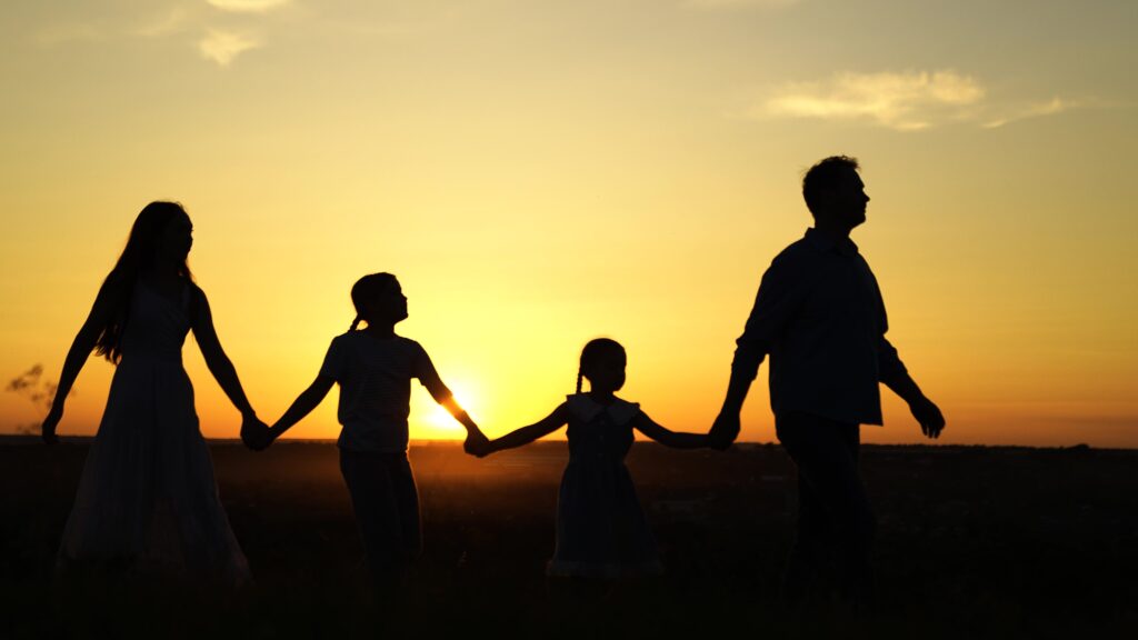 Family of four walking through field at sunset.