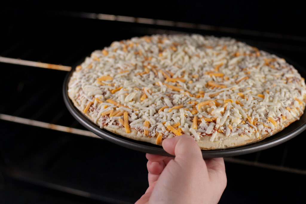 Frozen cheese pizza going into the oven